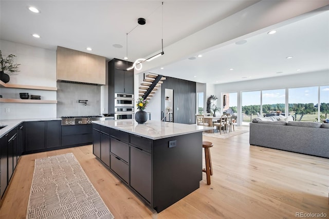 kitchen featuring a breakfast bar area, hanging light fixtures, light stone counters, a kitchen island, and light wood-type flooring