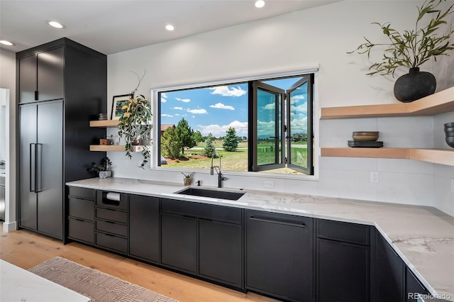 kitchen featuring high quality fridge, sink, light stone countertops, and light wood-type flooring