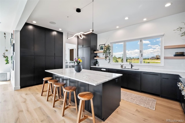 kitchen featuring sink, a kitchen breakfast bar, a center island, light stone counters, and light wood-type flooring