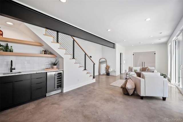 bar with tasteful backsplash, beverage cooler, concrete flooring, and sink