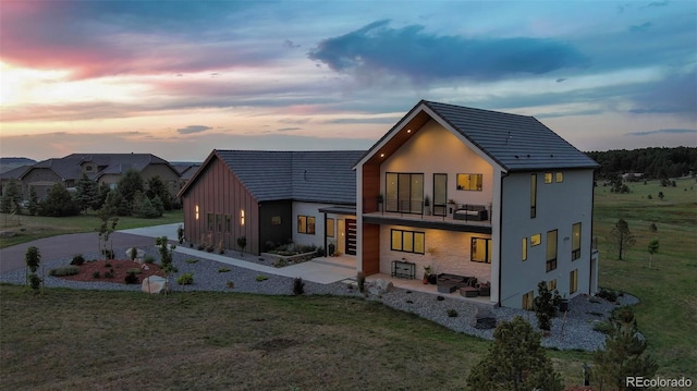 back house at dusk with a lawn and a balcony