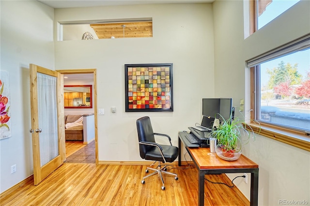 office with french doors, a high ceiling, and light hardwood / wood-style flooring