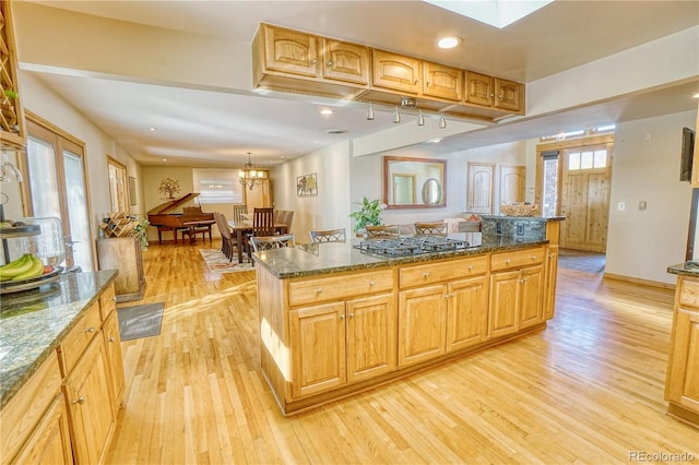 kitchen with light hardwood / wood-style flooring, a kitchen island, and dark stone counters