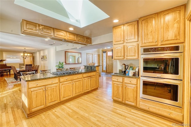 kitchen featuring appliances with stainless steel finishes, light wood-type flooring, a skylight, dark stone countertops, and a chandelier