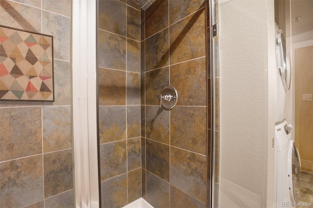 bathroom with a tile shower and stacked washer / dryer