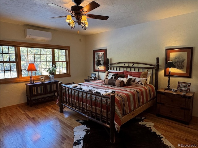 bedroom featuring hardwood / wood-style floors, a textured ceiling, a wall unit AC, and ceiling fan