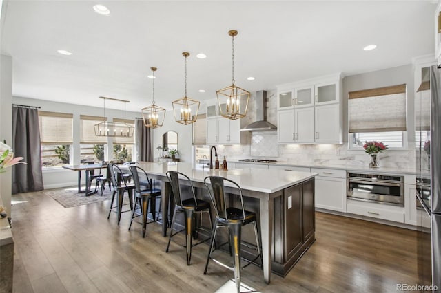 kitchen with a kitchen island with sink, stainless steel appliances, light countertops, wall chimney exhaust hood, and tasteful backsplash