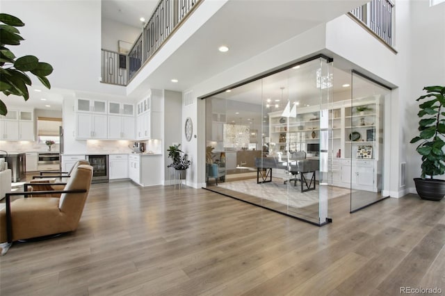 living room with wood finished floors, visible vents, baseboards, a high ceiling, and wine cooler