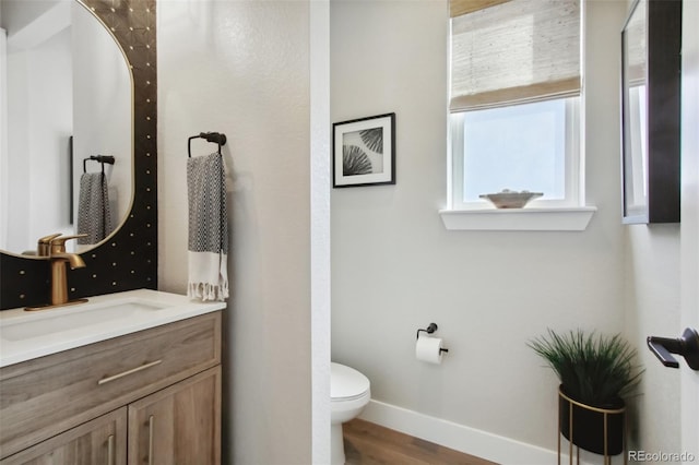 half bathroom featuring toilet, vanity, baseboards, and wood finished floors