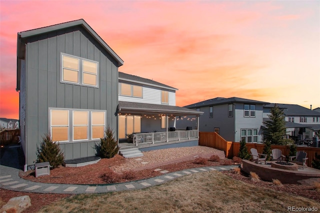 back of house at dusk featuring covered porch, board and batten siding, a shingled roof, and an outdoor fire pit