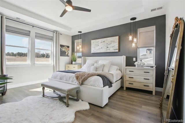 bedroom featuring a ceiling fan, dark wood-style floors, visible vents, baseboards, and a tray ceiling