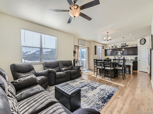 living room featuring ceiling fan with notable chandelier and light hardwood / wood-style floors