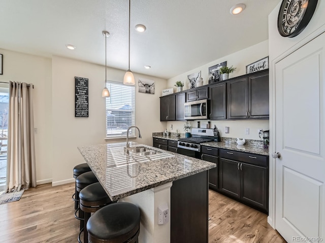 kitchen with appliances with stainless steel finishes, dark stone counters, pendant lighting, a center island with sink, and a breakfast bar area