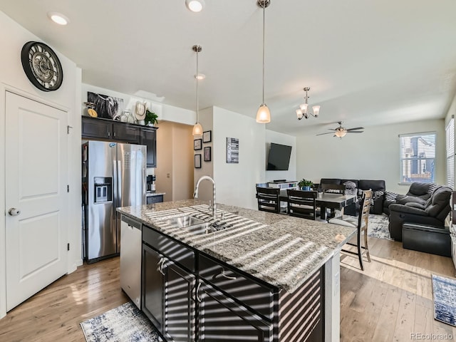 kitchen with ceiling fan with notable chandelier, sink, light wood-type flooring, an island with sink, and stainless steel appliances