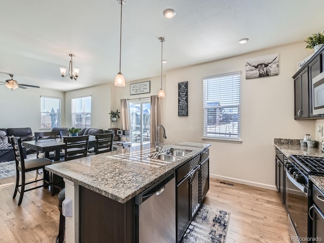 kitchen with pendant lighting, a center island with sink, ceiling fan with notable chandelier, a healthy amount of sunlight, and stainless steel appliances