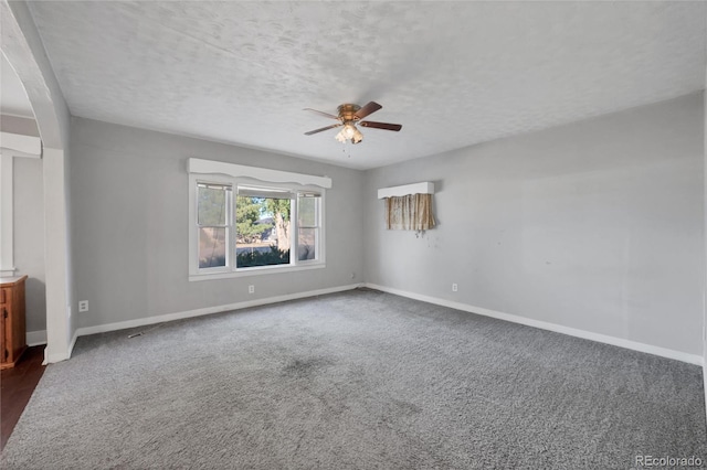 spare room with a textured ceiling, ceiling fan, and dark colored carpet