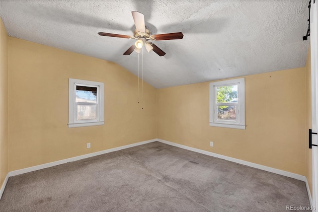 carpeted spare room featuring ceiling fan, vaulted ceiling, and a textured ceiling