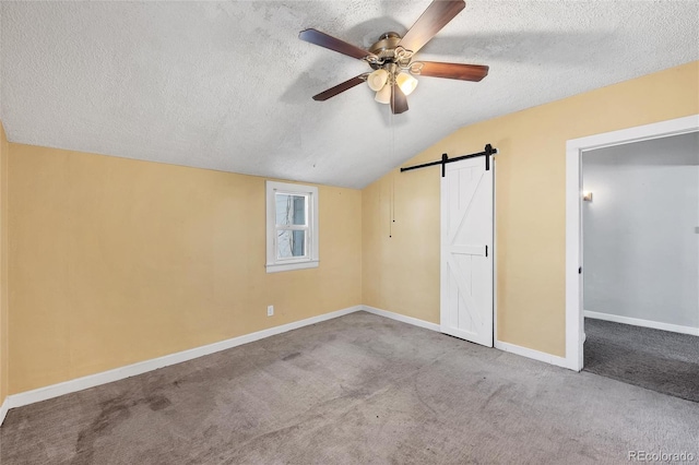 unfurnished bedroom with ceiling fan, a textured ceiling, light carpet, vaulted ceiling, and a barn door