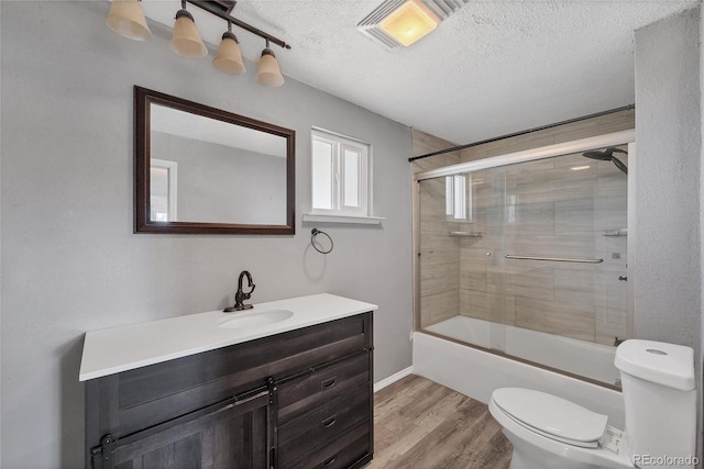 full bathroom featuring hardwood / wood-style floors, shower / bath combination with glass door, vanity, toilet, and a textured ceiling