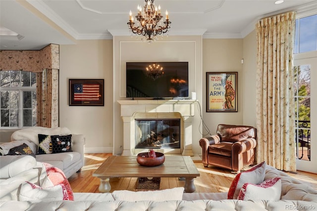 living area with crown molding, a glass covered fireplace, wood finished floors, a chandelier, and baseboards