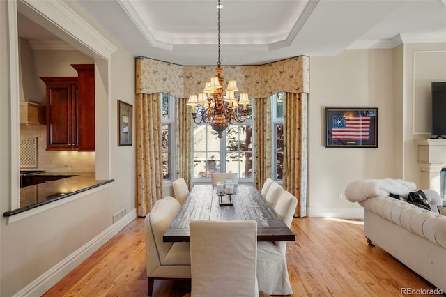 dining space featuring light wood-type flooring, a raised ceiling, visible vents, and baseboards