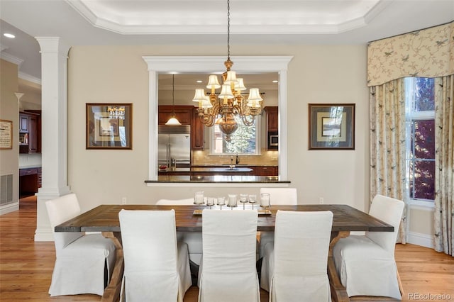 dining space featuring ornate columns, a raised ceiling, and light wood finished floors