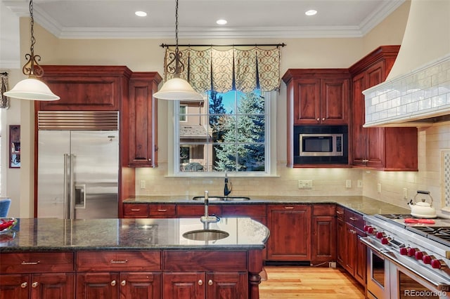 kitchen featuring reddish brown cabinets, crown molding, custom exhaust hood, a sink, and built in appliances