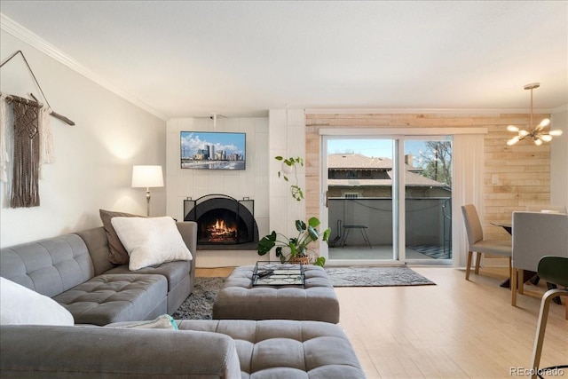 living area featuring a notable chandelier, ornamental molding, light wood finished floors, and a tile fireplace