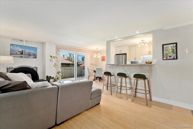 living room featuring a fireplace, light wood-type flooring, baseboards, a notable chandelier, and recessed lighting