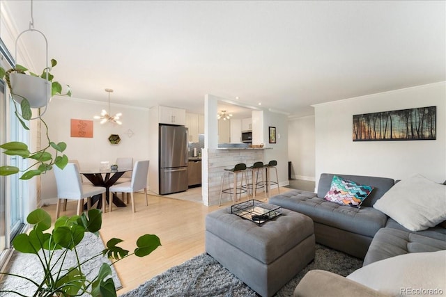 living area featuring an inviting chandelier, baseboards, crown molding, and light wood-style flooring