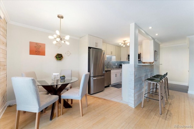 kitchen featuring a breakfast bar area, stainless steel appliances, crown molding, and an inviting chandelier