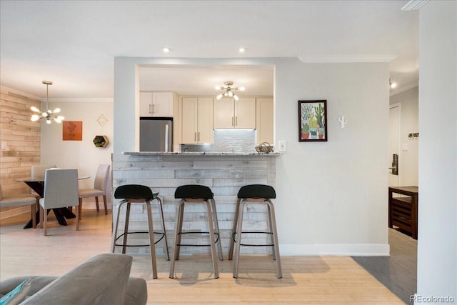 kitchen featuring a chandelier, stainless steel refrigerator, ornamental molding, and a kitchen bar