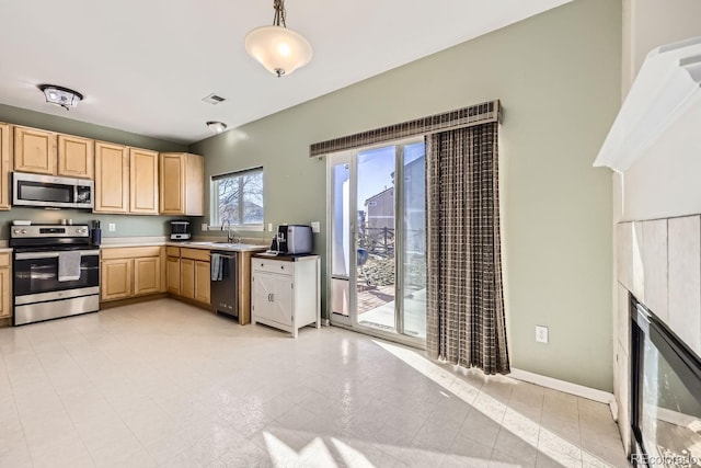 kitchen featuring sink, hanging light fixtures, a tiled fireplace, stainless steel appliances, and light brown cabinetry