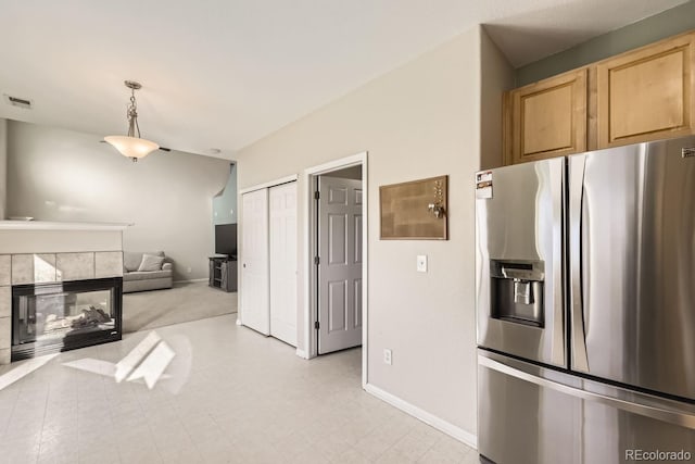 kitchen featuring stainless steel fridge with ice dispenser, light brown cabinetry, a tile fireplace, and decorative light fixtures