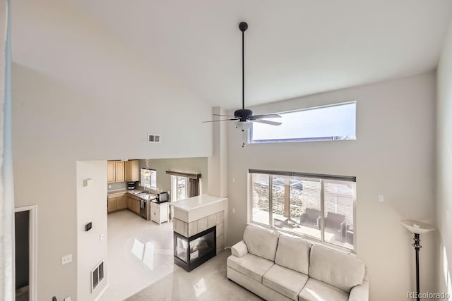 living room with ceiling fan, a towering ceiling, and a fireplace