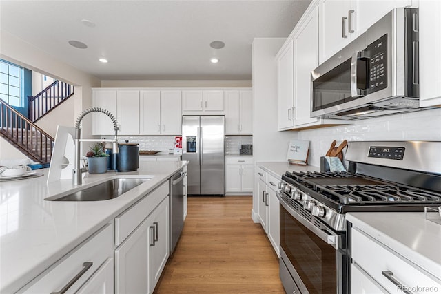 kitchen with appliances with stainless steel finishes, white cabinetry, sink, decorative backsplash, and light hardwood / wood-style flooring