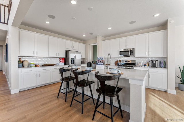 kitchen with white cabinetry, a kitchen island with sink, a kitchen breakfast bar, and appliances with stainless steel finishes