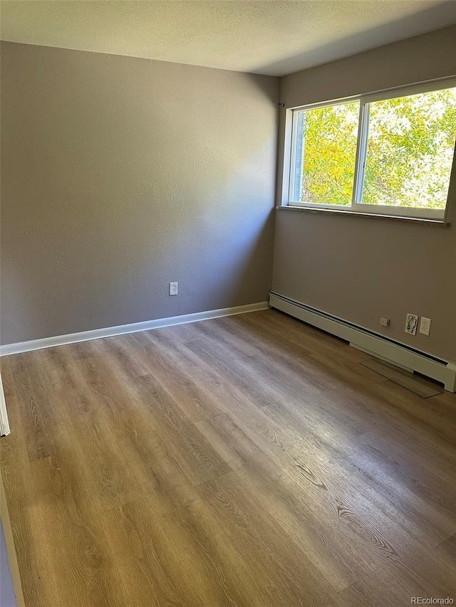 empty room featuring a baseboard heating unit, light hardwood / wood-style flooring, and a textured ceiling