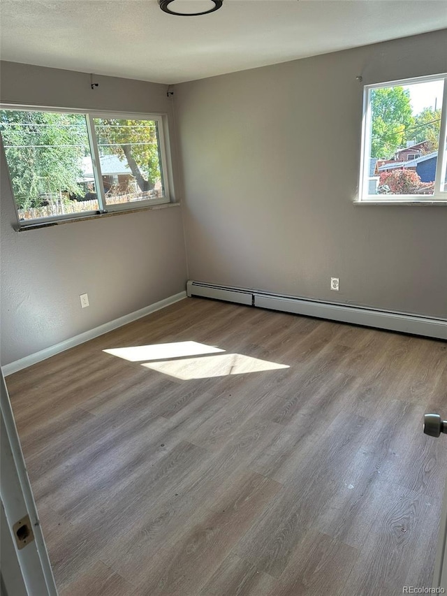 unfurnished room featuring plenty of natural light, baseboard heating, and light wood-type flooring