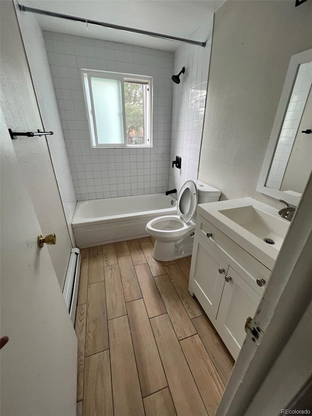 full bathroom featuring vanity, toilet, tiled shower / bath, and baseboard heating