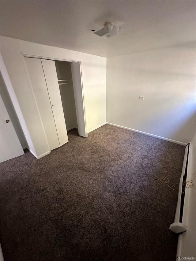 unfurnished bedroom featuring dark carpet and a closet