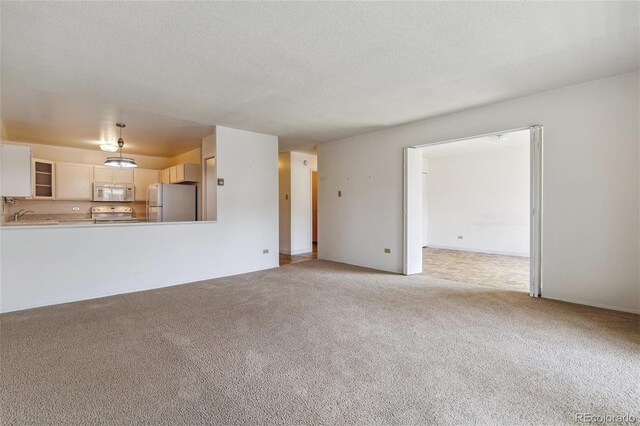 unfurnished living room with light carpet, sink, and a textured ceiling