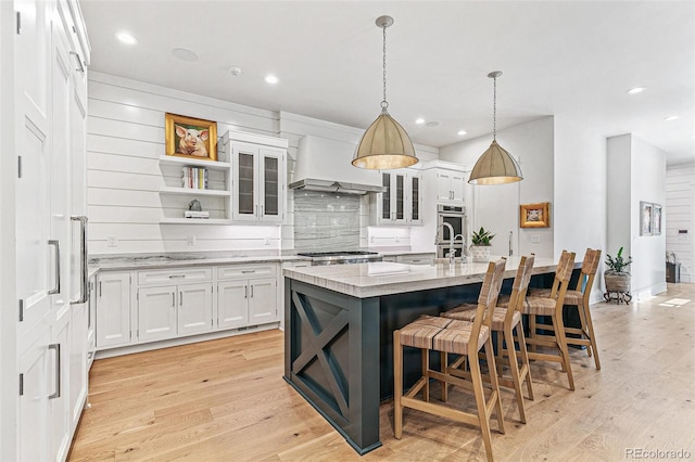 kitchen with light hardwood / wood-style floors, white cabinets, stainless steel appliances, decorative light fixtures, and a center island with sink