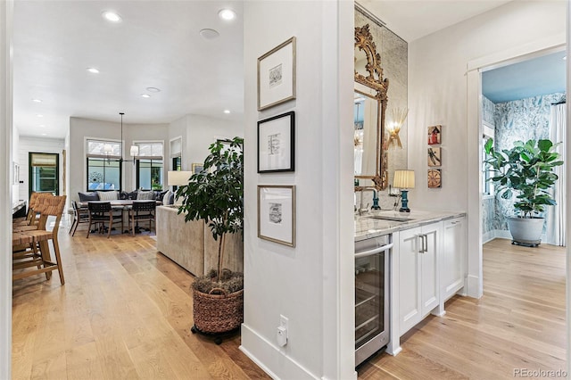 corridor with a notable chandelier, beverage cooler, sink, and light hardwood / wood-style floors