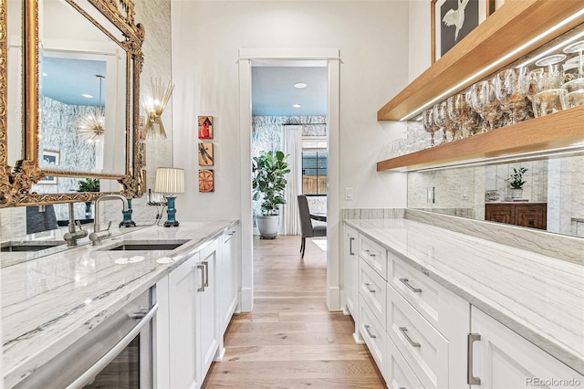 kitchen with light hardwood / wood-style flooring, light stone counters, white cabinetry, and sink