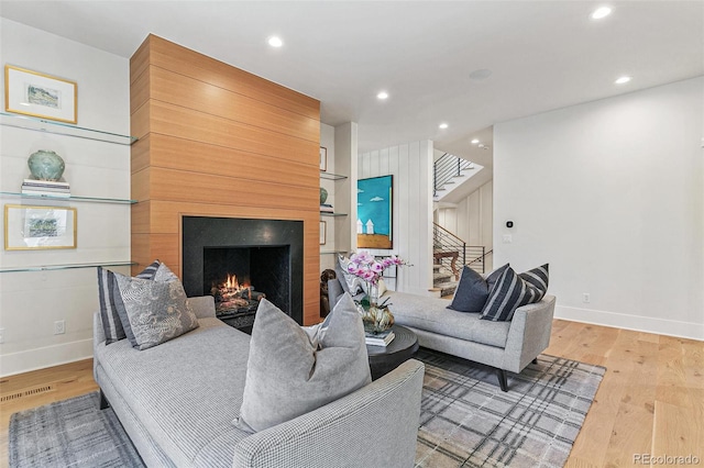 living room with a large fireplace, hardwood / wood-style flooring, and wooden walls