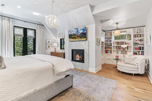 bedroom with light wood-type flooring, a fireplace, vaulted ceiling, and an inviting chandelier