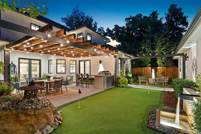 back house at dusk with a patio, a pergola, exterior bar, and an outdoor kitchen