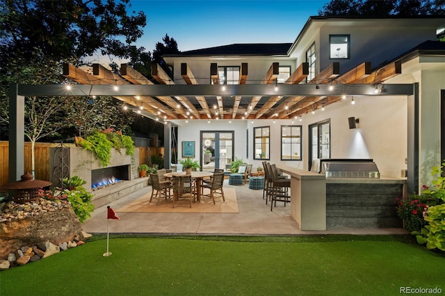 back house at dusk featuring a pergola, area for grilling, exterior bar, and a patio area