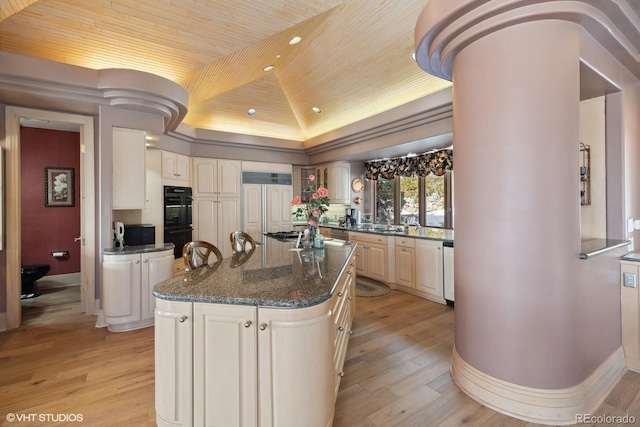 kitchen featuring a center island, light hardwood / wood-style flooring, double oven, dark stone countertops, and lofted ceiling